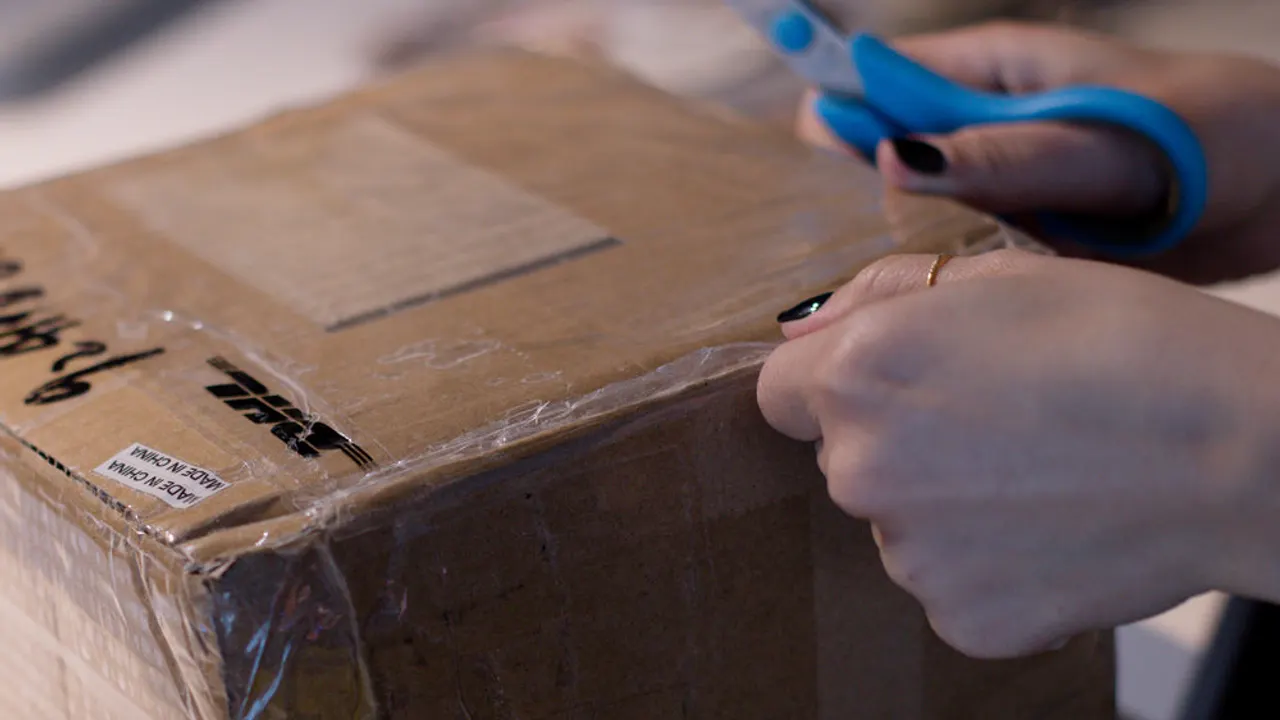 Taped up cardboard box with a person holding scissors.