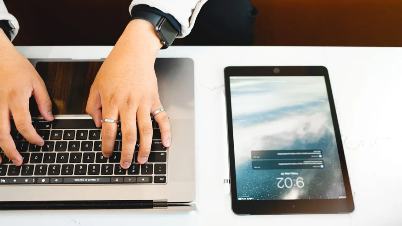 Hands type on a laptop that is next to a tablet.
