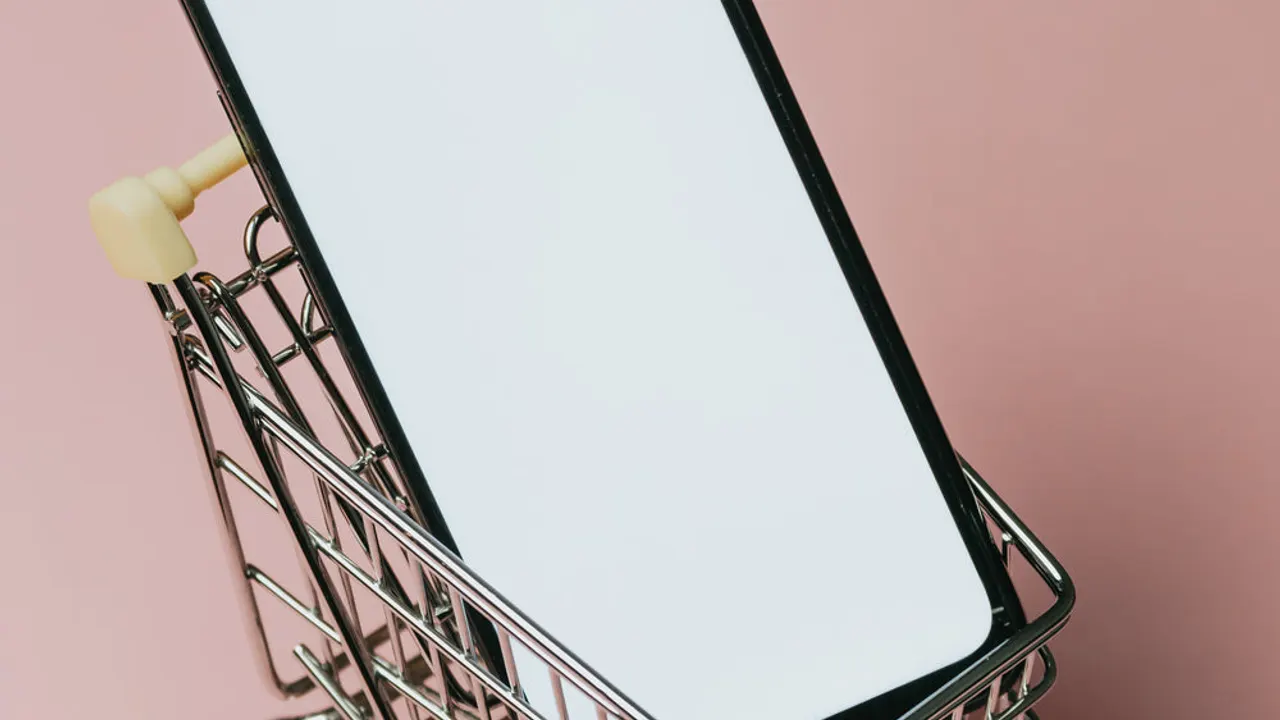 Black cell phone in a small silver shopping cart.